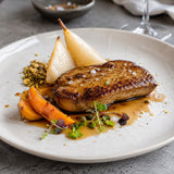 A plated gourmet dish featuring a slice of pan-fried foie gras escalope, served with pears, peach slices, and microgreens.