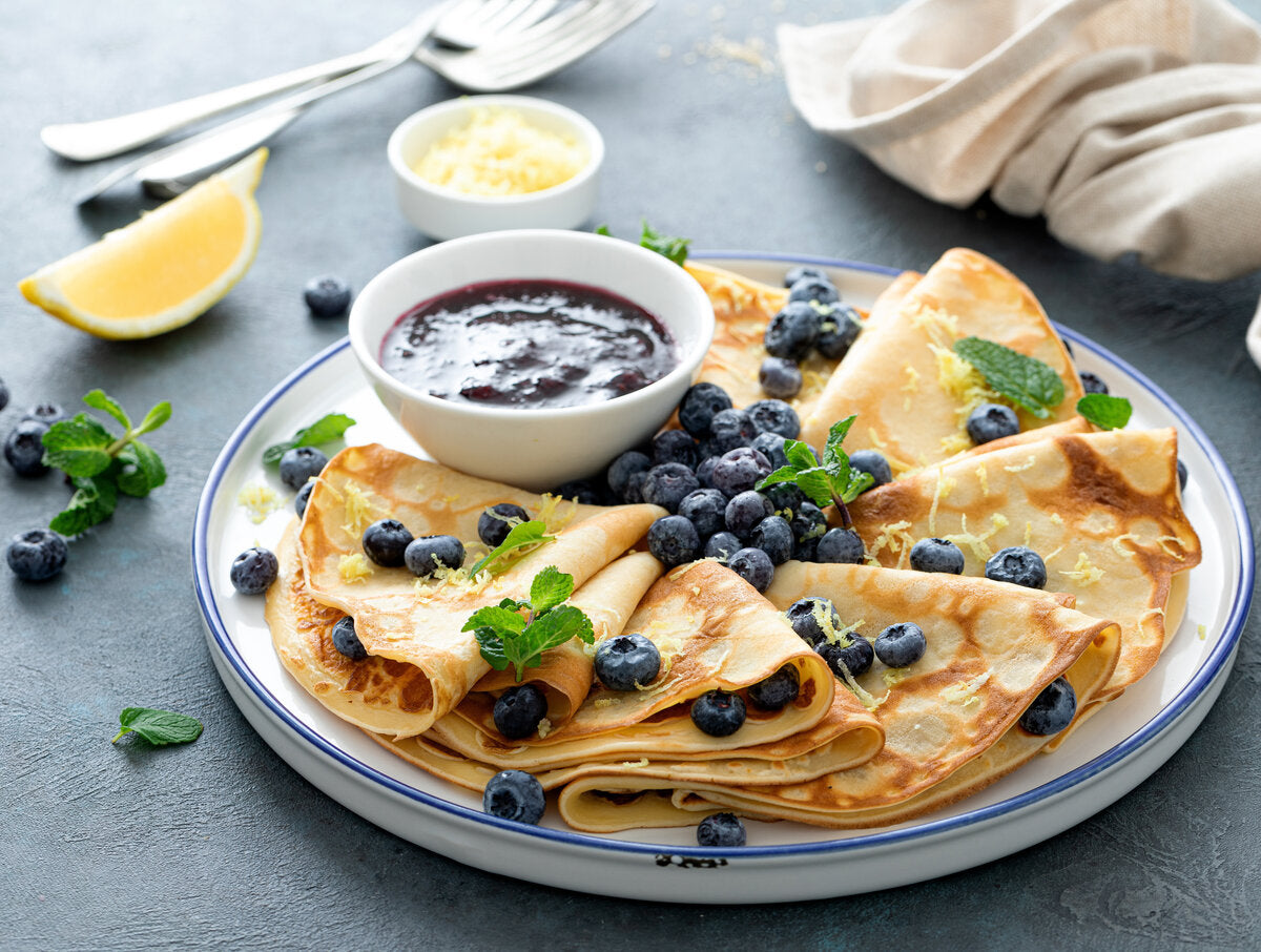 Stack of crepe-style pancakes with blueberries and a side of healthy blueberry jam on a plate.