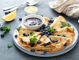 Stack of crepe-style pancakes with blueberries and a side of healthy blueberry jam on a plate.