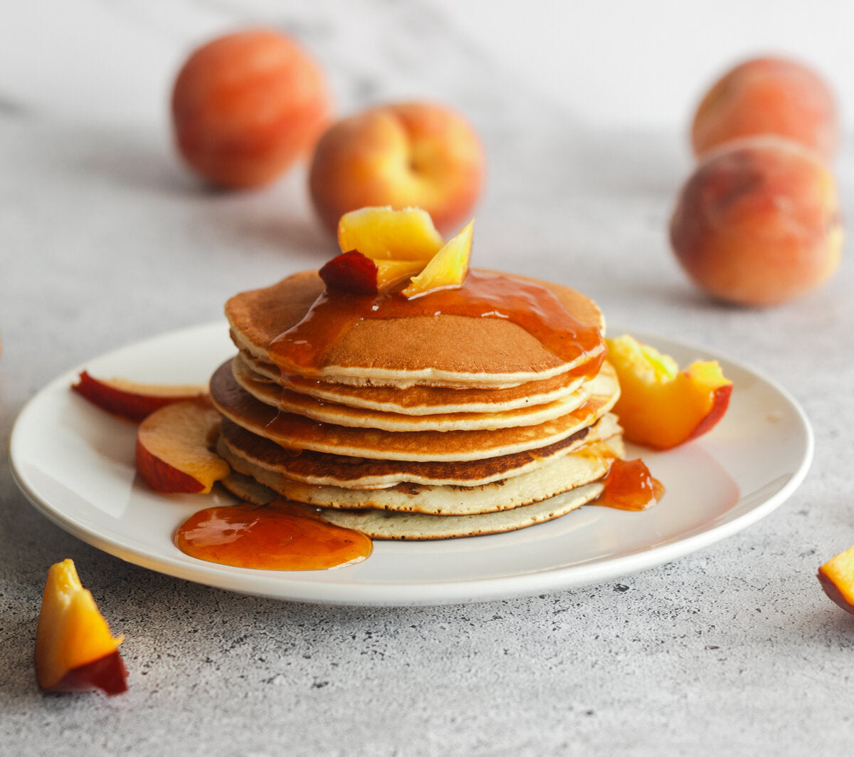 Stack of pancakes with peach jam and fresh peach slices on a white plate.