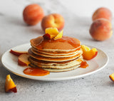 Stack of pancakes with peach jam and fresh peach slices on a white plate.