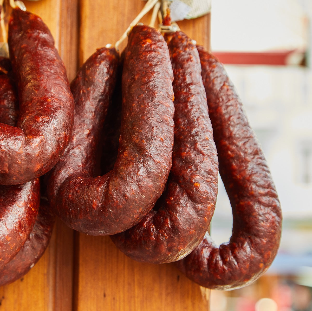 String of dried paraszt kolbász Hungarian sausages hanging on a wooden board.