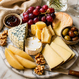 Cheese board featuring an assortment of cheeses with grapes, pear compote slices, walnuts, olives and chutney.
