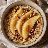 Creamy oatmeal topped with three slices of pear compote, walnuts, and a dusting of cinnamon, set on a neutral fabric surface.