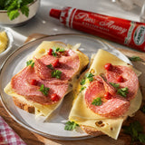 Two sandwiches with salami and cheese on a plate, with a tube of Piros Arany in the background.