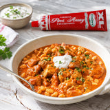 Bowl of Hungarian paprikash with a tube of Piros Arany on a wooden table.