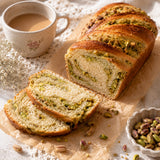 Loaf of pistachio babka bread with slices cut, served with a cup of coffee and raw pistachios by the side.