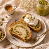 Two slices of pistachio babka cake on a plate with a cup of milk and jar of pistachio cream.