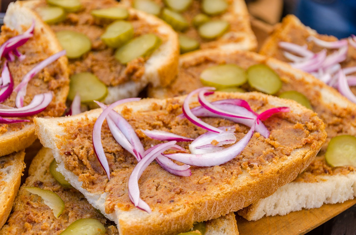 A slice of bread topped with a pork greaves spread, red onions and gherkins.