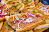 A slice of bread topped with a pork greaves spread, red onions and gherkins.