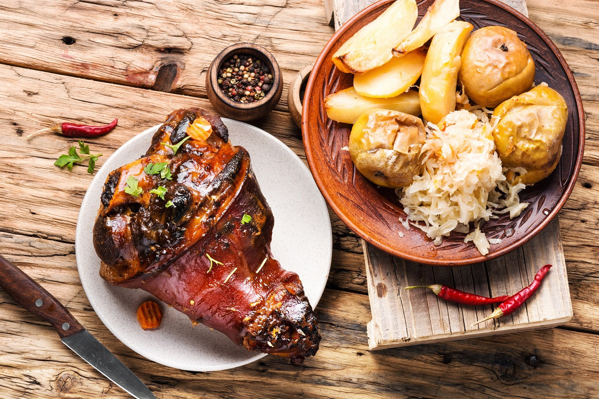 Roasted pork ham hock with potatoes and sauerkraut on a wooden table.