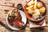 Roasted pork ham hock with potatoes and sauerkraut on a wooden table.