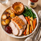 Roast pork with potatoes, roasted vegetables, Yorkshire pudding and quince jam on a wooden table.