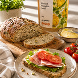 Loaf of pumpkin seed bread with a sandwich on a plate and a bag of ground pumpkin seeds.