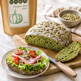 Loaf of pumpkin seed bread with a sandwich on a plate and a bag of pumpkin seed flour.