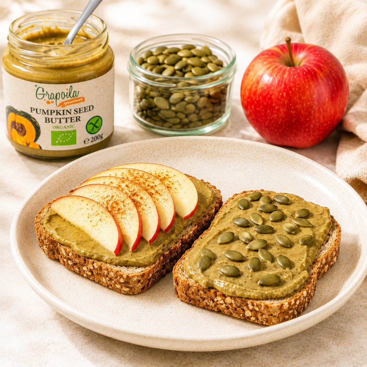 Two slices of bread with pumpkin seed spread, apples, and pumpkin seeds on a plate, with a jar of pumpkin seed butter in the background.