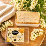 A piece of pure and natural raw honeycomb in a tin on a wooden surface with acacia flowers around.