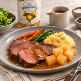 Sliced roast beef with gravy, mashed potato, carrots, green beans, and cubes of quince compote on a ceramic plate.