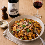 Plate of beef ragu with pappardelle pasta, basil and grated Parmesan, paired with a bottle of Tricollis red wine.