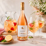 A bottle of Szentpeteri rose wine with glasses and a fruit cocktail made with lemonade on a table.