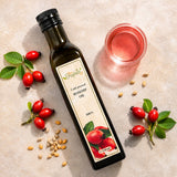 Glass of rosehip oil next to rosehip seeds and red rosehip berries on a light surface