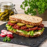 Sandwich with spicy salami, pickles, and lettuce on a black slate board with radishes and parsley.