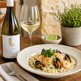 A dish of seafood risotto with a bottle of Sauvignon Blanc and a glass of white wine on a table.
