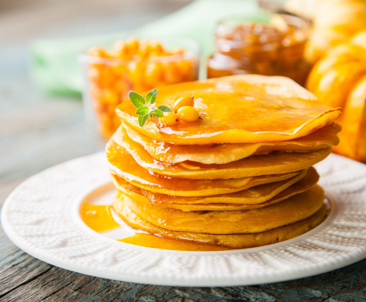 Stack of pancakes with sea buckthorn berry compote in syrup on a white plate.