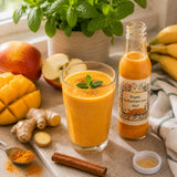 Orange smoothie in a glass with a bottle of sea buckthorn juice, mangoes, apples, ginger, and cinnamon.