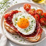 Fried egg on toast with sliced ham and tomatoes on a white plate.