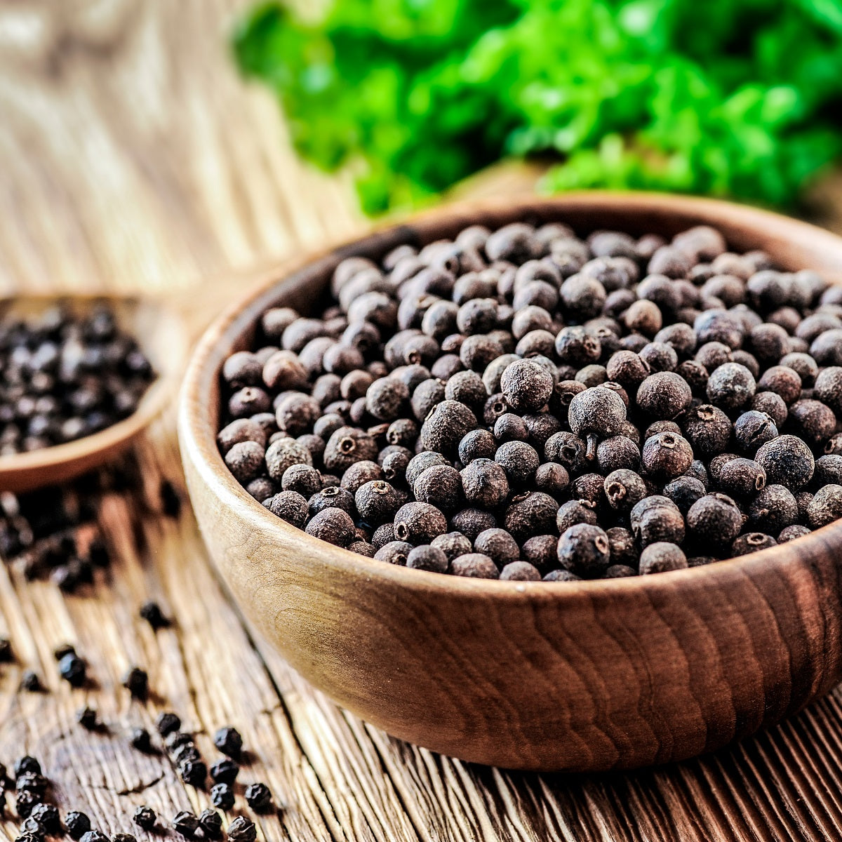 Wooden bowl filled with smoked black peppercorns on a wooden surface.