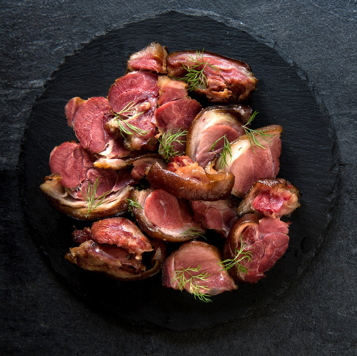 Sliced roasted smoked pork ham hock meat with herbs on a dark slate surface