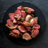Sliced roasted smoked pork ham hock meat with herbs on a dark slate surface