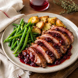 A plate of roasted duck breast with a sour cherry jam sauce, steamed green beans and roast potatoes.