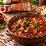 A ceramic bowl filled with a spicy beef and potato goulash with a tube of Hot Hungarian Goulash Paste.