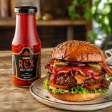 Burger with bacon and cheese on a plate next to a bottle of Rex Spicy Ketchup on a wooden table.