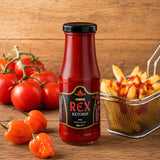 Bottle of Rex Spicy Ketchup with fries, tomatoes and habanero peppers on a wooden surface.