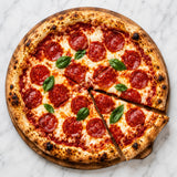 Spicy salami pizza with cheese and basil leaves on a marble surface.