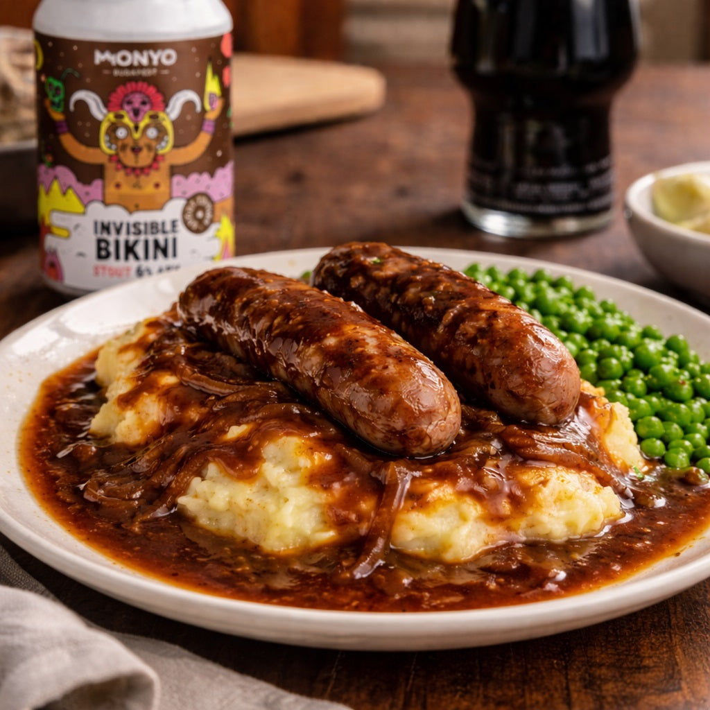 Plat of sausages, mash and peas in a thick gravy made from stout beer on a wooden table with a can in the background.