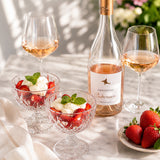 A bottle of rosé wine with two glasses, paired with dessert bowls with strawberries and cream.