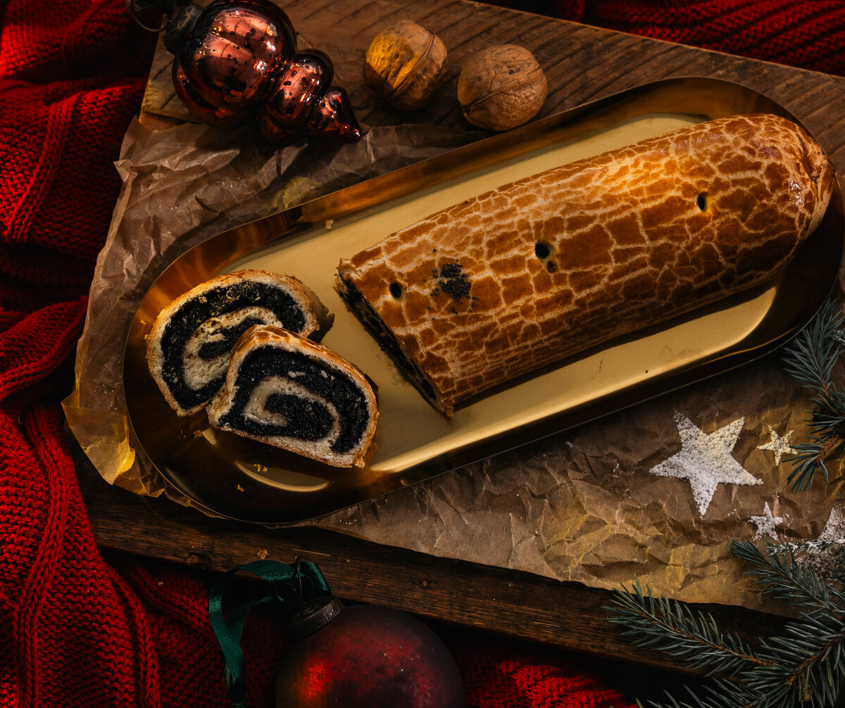 A Strudla sa makom poppy seed roll on a gold tray with Christmas ornaments and a red fabric background
