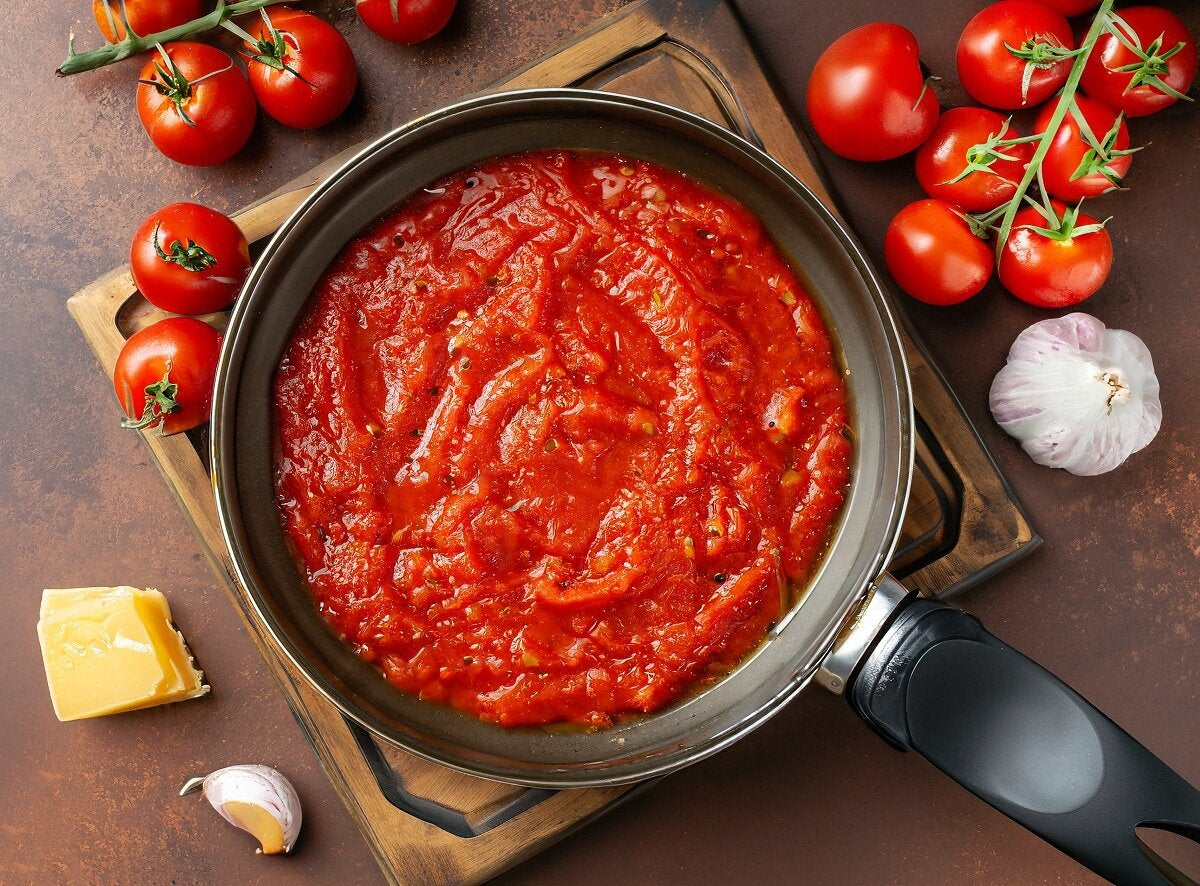 A pasta sauce in a saucepan made from tomato concentrate, with fresh tomatoes, garlic and cheese.