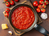 A pasta sauce in a saucepan made from tomato concentrate, with fresh tomatoes, garlic and cheese.