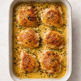 Baked chicken thighs in a creamy truffle mustard sauce with herbs in a metal baking dish.