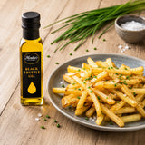 Bottle of black truffle oil next to a plate of fries on a wooden surface.