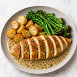 Plated dish with sliced roasted chicken in a truffle pesto sauce, roasted potatoes, and broccolini.