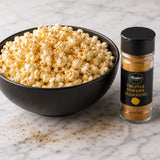 Bowl of popcorn with a bottle of truffle powder seasoning on a marble surface.