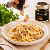 Pasta dish with black truffle pieces being sliced over it, with a jar of whole truffles in the background.