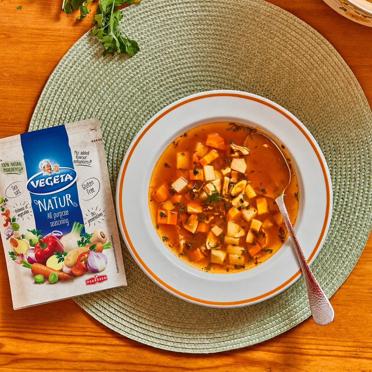 Vegetable soup in a bowl with a Vegeta seasoning packet on a wooden table.