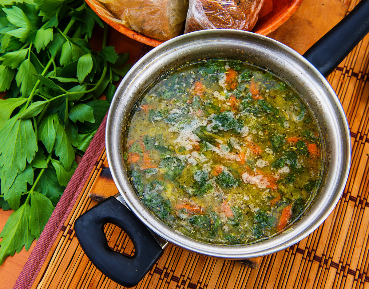 Potted vegetable soup with lovage and carrots on a wooden table.